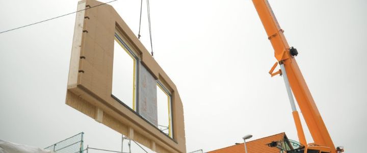 Vorgefertigtes Wandelement hängt am Kran über der Baustelle